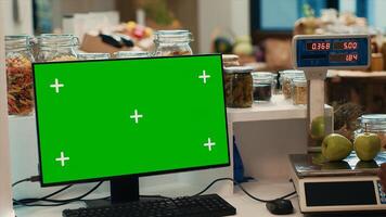 Greenscreen monitor on counter at local bio farmers market, shopper looking for homegrown ethically sourced produce. Blank copyspace chromakey display on computer at supermarket. photo