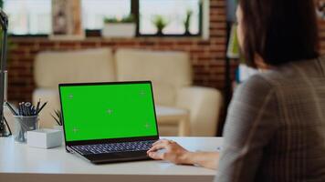 Freelancer checking emails on green screen laptop during work from home at computer desk. Self employed woman in cozy bright apartment doing job tasks, reading business messages on mockup device photo