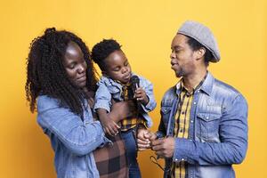 African american mom and dad teaching their son how to sing in studio, learning to perform songs on microphone from a young age. Adorable little boy singing a new melody in front of the camera. photo