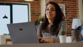Portrait of smiling teleworker checking her emails on notebook device while at computer desk. Remote worker inputting data on laptop in bright stylish cozy apartment personal office, solving tasks photo