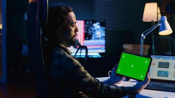 Freelancer holding isolated screen tablet, analyzing statistical charts on laptop in living room. Remote employee checking business revenue numbers on chroma key electronic device photo