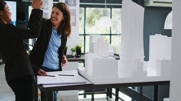 Architects team sharing high five after making progress with their remodeling project, real estate agency employees collaborating to execute project plans. CAD experts designing blueprints. photo