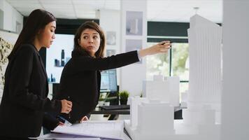 Cad experts examining architectural blueprints at agency, holding 3d printed building model to measure elements and shapes. Team of women architects studying property scale draft, coworking space. photo