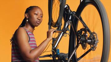 BIPOC engineer checking bicycle performance by spinning pedals. Skilled specialist ensuring proper function of tires on bike wheels in orange studio background during maintenance, camera A photo