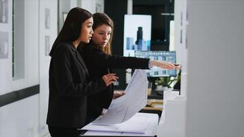 Startup team working with architectural blueprint plans, studying scale measurements and technical elements in coworking space. Woman architects looking at 3d maquette building model. photo
