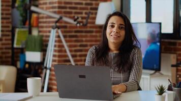 Portrait of indian teleworker checking her emails on laptop while at computer desk. Remote employee working from home in bright stylish cozy apartment personal office, solving tasks, zoom in, camera B photo