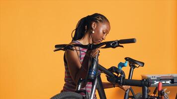BIPOC mechanic setting up bike repair stand, using it to adjust handlebar and fix broken wheels, studio background. Professional placing bicycle on workstand in tight grip to inspect it, camera A photo