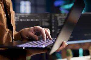 Computer scientist working from home using laptop, testing and deploying programs. Programmer checking code displayed on desktop PC screens in blurry background, close up shot photo