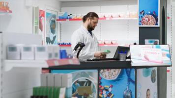 Male pharmacist using scanner to register new stock at counter, working at pharmacy checkout to ensure medicaments and supplements inventory. Employee scanning pharmaceutics in store. photo