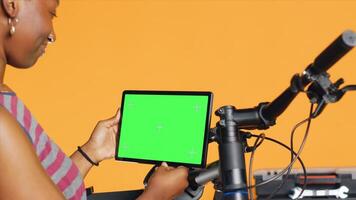 Mechanic doing bike servicing in studio background atelier shop, looking on isolated screen tablet maintenance list. Specialist checks online for replacement bicycle parts on mockup electronic device photo