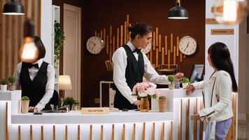 Asian guest arriving at hotel and asking about room reservation, talking to receptionist about check in process. Front desk staff team greeting customer at reception, presenting leisure facilities. photo