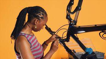 African american engineer uses screwdriver to unmount bicycle handlebars, testing components quality in studio background repair shop. Professional unscrewing bike parts in order to fix them, camera A photo