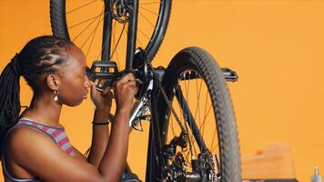 Engineer pushing pedals to rotate bike wheel, inspecting it and using screwdriver and hex socket wrench to fix it. Professional testing bike crank arm and chain rings, camera A photo