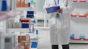 Druggist counting all pharmaceutical stock in pharmacy shop, working on inventory with checklist on clipboard. Pharmacist examining medical products on drugstore shelves. Camera 2. photo