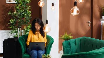 Asian tourist creating trip itinerary to visit landmarks, using internet while she waits for check in process. Hotel guest arriving early at reception, searching for famous places on laptop. photo