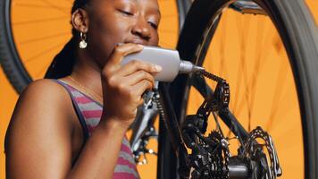 Experienced serviceman using specialized glue to mend defective bicycle chain, orange studio background. Worker applying adhesive on bike parts during inspection process, close up shot photo
