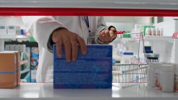 POV of pharmacist putting products from shelves in the basket, reorganizing medicaments based on types and uses. Healthcare worker taking off boxes of pharmaceuticals from racks. Tripod shot. photo