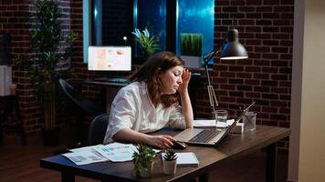 Businesswoman working overtime for company project, doing tasks in office overnight, struggling to remain awake. Tired employee yawning while looking over data on laptop screen late at night, camera A photo