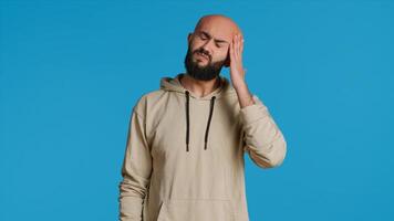 Unwell arab model dealing with serious headache in studio, feeling sick with a painful migraine and rubbing temples to ease the pressure. Tired person suffering from pain and tension. Camera 1. photo