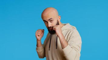 Muslim male model acting aggressive with clenched fists, preparing to fight and punch someone on camera. Arab person being violent and boxing in studio, strong man with fighter pose. Camera 2. photo