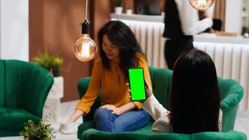 Customer looking at greenscreen layout on phone display, waiting for check in at hotel. Asian woman sitting on couch with smartphone showing blank copyspace mockup layout. Tripod shot. photo