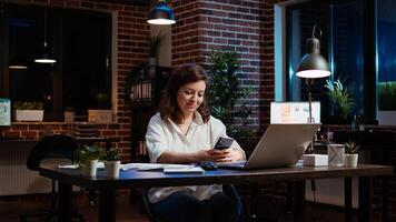 Smiling manager looking at text messages on smartphone, taking break from working on company project. Team leader unwinding by using phone to browse social media in office, camera A photo