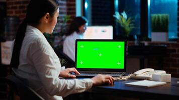 Worker looking over green screen laptop display, researching key data for company project. Businesswoman analyzing figures and charts on chroma key electronic device in office at night photo