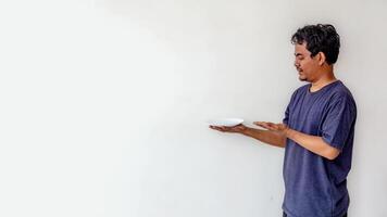 Adult man holding an empty white plate while pointing at it, as if presenting food, isolated on a white background. Perfect for themes related to cooking, dining, food presentation. photo