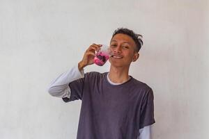 A young man wearing a gray t-shirt and glasses is enjoying an Indonesian mixed iced drink or holding a plastic cup isolated on white background. for food content and health, and diabetes concepts photo