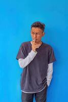 a young man wearing a gray t-shirt smoking isolated on blue background. suitable for health and environmental concepts photo