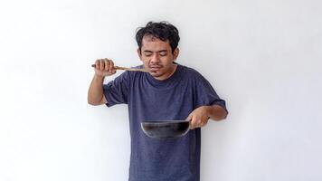 Adult man tasting food with a wooden spatula while holding a frying pan, isolated on a white background. Ideal for themes related to cooking, food preparation, and culinary skills. photo