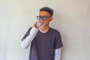 a young man wearing a gray t-shirt with glasses is smoking isolated on white background. suitable for health and environmental concepts photo