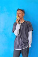 Young expressive singer happy man wearing gray t-shirt with glasses and hat singing song into microphone spreading hands isolated on plain light blue background studio. People's lifestyle concept photo
