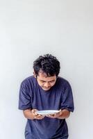 Adult man holding and looking at an empty white plate with a hungry expression, depicting poverty isolated on a white background for themes related to hunger, food scarcity, and social issues. photo