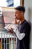 a young man wearing a gray t-shirt with glasses is smoking while holding a smartphone. suitable for health and environmental concepts photo