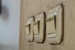 Three vintage light switches on a textured wall, showing signs of wear and tear. photo