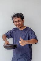 an adult man holding or lifting a frying pan while giving a thumbs up like a chef shows that the food is delicious isolated on white background photo