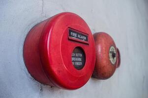 Retro fire alarm components attached to a white wall, such as a red break glass button and a bell. photo