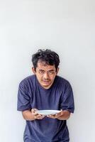 Adult man holding and looking at an empty white plate with a hungry expression, depicting poverty isolated on a white background for themes related to hunger, food scarcity, and social issues. photo