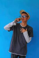 Young expressive singer happy man wearing gray t-shirt with glasses and hat singing song into microphone spreading hands isolated on plain light blue background studio. People's lifestyle concept photo
