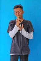 Young expressive singer happy man wearing gray t-shirt with glasses and hat singing song into microphone spreading hands isolated on plain light blue background studio. People's lifestyle concept photo
