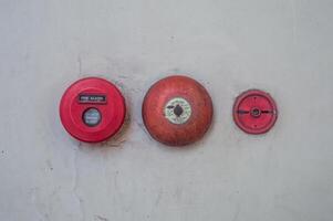 Retro fire alarm components attached to a white wall, such as a red break glass button and a bell. photo