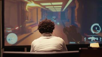 Man playing first person shooter videogame on smart TV in futuristic industrial setting with health, stamina, ammo bars HUD overlay. Gamer enjoying competitive PvP fps online multiplayer game photo