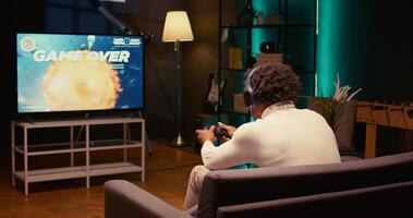 Gamer receiving game over screen on ultrawide smart TV, losing all health, failing to win level and beat enemies. BIPOC player defeated in science fiction singleplayer videogame, panning shot photo