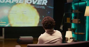 Upset african american gamer raging after losing game, playing on ultrawide smart TV. Man in living room feeling angry and shouting after his spaceship exploded, defeated in videogame photo