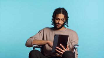 Man in wheelchair chatting with friend over internet videocall using tablet. Person with disability holding portable device, discussing with mate in teleconference, studio background, camera A photo
