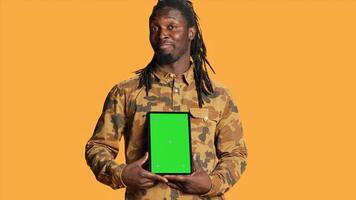 African american adult with greenscreen on gadget, presenting isolated chromakey display and smiling in front of camera. Young adult holding mobile device with copyspace blank layout. photo