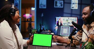 Woman and man participating in podcast, laughing while watching funny internet clips on green screen tablet in studio, discussing content. Podcasters reacting to amusing videos on chroma key device photo