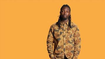 African american man with camo shirt posing in studio, smiling and feeling confident over orange background. Young male model feeling joyful and excited on camera, expressing positivity. photo