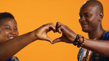 Ethnic couple in love showing heart shape sign and kissing in front of camera, sharing their affection and sincere feelings. Romantic people share kiss in studio, presenting love symbol. Close up. photo